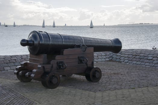 cannon in the harbor with boats on the background