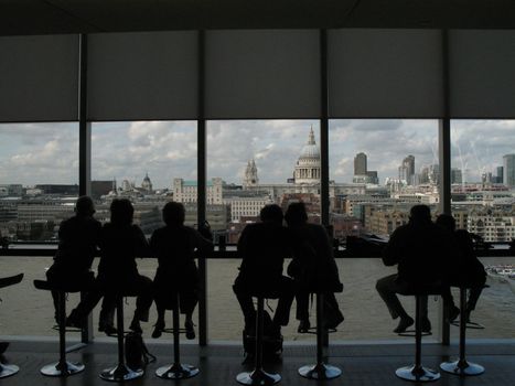 people silhouettes at the bar in the art gallery with a panoramic view of London and the Thames river on a cloudy day