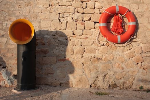 street view with a waste disposal in unusual form of boat pipe and a safety ring on a stony wall