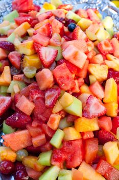 A healthy platter of fruit at a wedding buffet. This image is in color and a vertical composition. It includes strawberries, watermelon, pineapple, honeydew, melon, grapes, blueberries, and more.