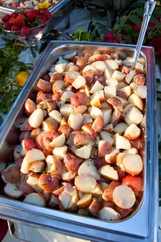 A serving dish of cooked potatoes and a serving spoon in the buffet line of a wedding reception. The meal looks healthy and delicious.