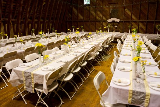 Tables are set up in an old barn for a wedding reception including dinner. These rows of tables are ready to seta and serve plenty of guests at this elegant diy wedding in the country.