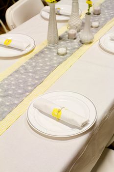 Silverware is wrapped up in a napkin for a wedding dinner reception in an old barn. The wedding decor includes a japanese or chinese influence with colors of white, grey (or gray) and yellow. They used twine to wrap up the place settings.