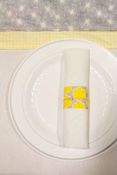 Silverware is wrapped up in a napkin for a wedding dinner reception in an old barn. The wedding decor includes a japanese or chinese influence with colors of white, grey (or gray) and yellow. They used twine to wrap up the place settings.