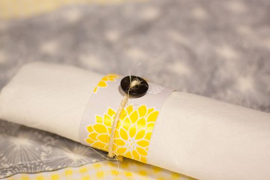 Silverware is wrapped up in a napkin for a wedding dinner reception in an old barn. The wedding decor includes a japanese or chinese influence with colors of white, grey (or gray) and yellow. They used twine to wrap up the place settings.