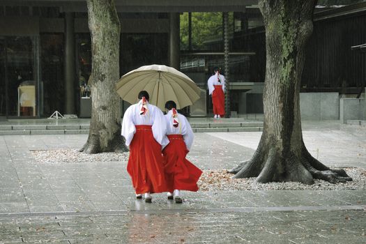 Japanese temple yard with girls in traditional clothing walking under heavy rain