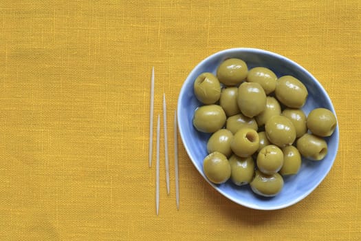 pitted green olives on blue plate over yellow tablecloth