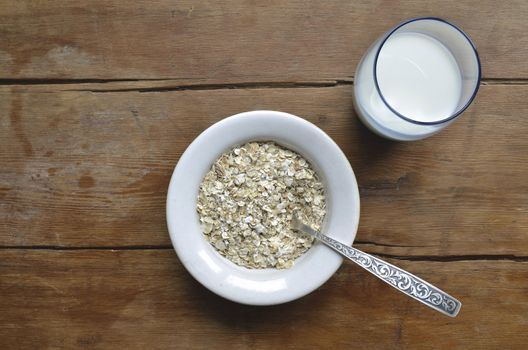 oat-flakes in white bowl and milk in blue glass on the vintage wooden table