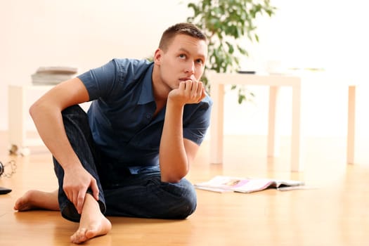 Portrait of handsome young man thinking at home on the floor