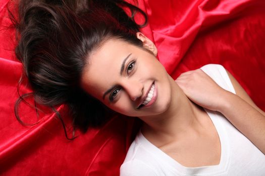 Closeup of beautiful and young brunette girl face lying on red matter