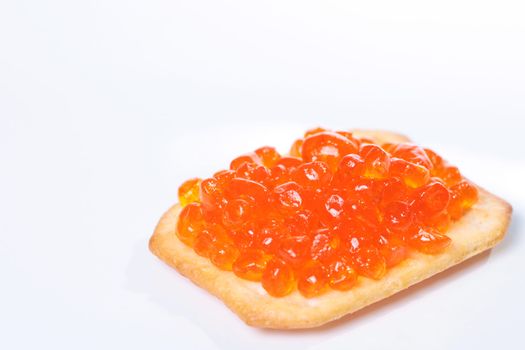 Close up of red tasty caviar on a cracker over a white background