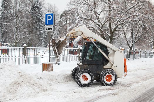 small excavator bobcat working on the street, cleaning snow