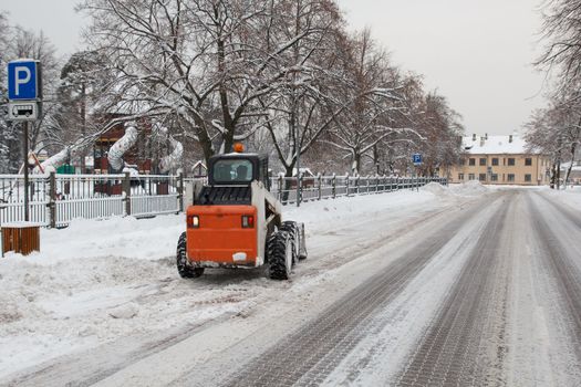 small excavator bobcat working on the street, cleaning snow
