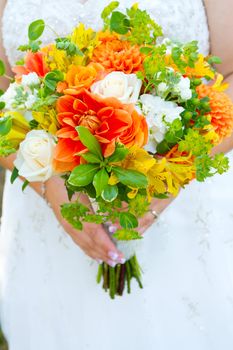 A bride in her white wedding dress holds her bouquet of orange, green, and yellow flowers on her wedding day.