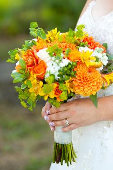 A bride in her white wedding dress holds her bouquet of orange, green, and yellow flowers on her wedding day.