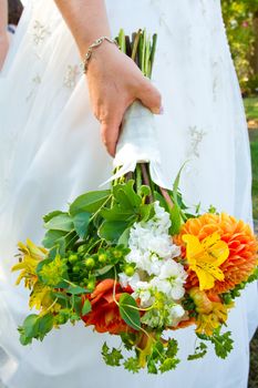 A bride in her white wedding dress holds her bouquet of orange, green, and yellow flowers on her wedding day.