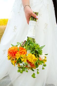 A bride in her white wedding dress holds her bouquet of orange, green, and yellow flowers on her wedding day.