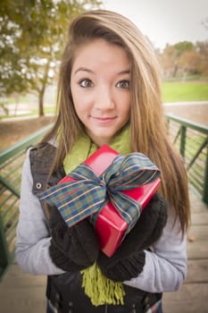 Pretty Festive Smiling Woman with Wrapped Gift with Bow Outside.