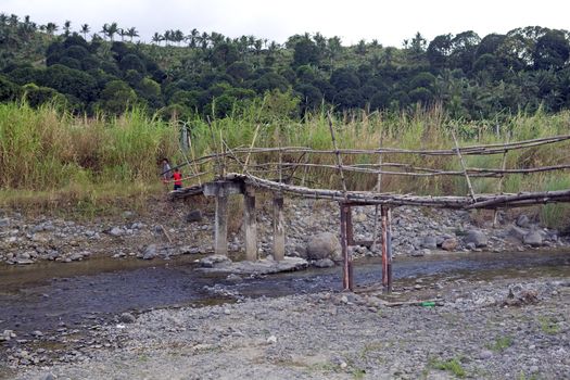 A small bamboo bridge crosses a river in a remote village in the Philippine Islands.