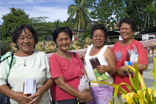 April 2012 - Bogo City, Panay, Philippine Islands - Four senior age Filipino christian women selling devotional candles outside the local Catholic church in Bogo City, Panay, Philippine Islands.