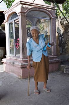May 2012 - Bogo City, Cebu Island, Philippines - Elderly, blind Filipino woman walking with a cane selling votive candles near a Catholic christian shrine. Senior citizens are held in high respect in the Philippine culture no matter how old they are.