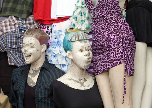 Two mannequin dummies outside a clothing store posed in a funny way. One is looking at the crotch of another dummy in a purple dress and the other is laughing.