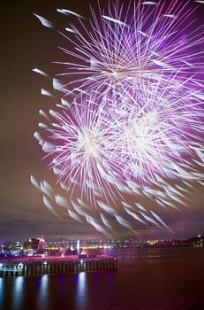 Montreal, Quebec, Canada - Night fireworks display strong wind feathering some of the bursts like horsetails. Jacques Cartier bridge visible in the distance.