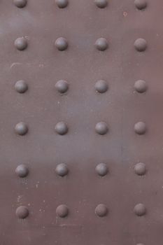 Background -  brown, rusty metal plate with vertical and horizontal rows of rivet heads.