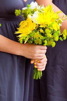 A bridesmaid in a navy blue grey dress holds her bouquet of yellow and green flowers at a wedding.