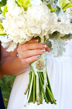 A bride holding her bouquet of flowers at her wedding ceremony with a meaningful brooch on the wrapping of the stems.