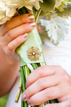 A bride holding her bouquet of flowers at her wedding ceremony with a meaningful brooch on the wrapping of the stems.