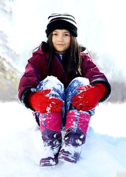 Little biracial girl sitting on top of snow in winter