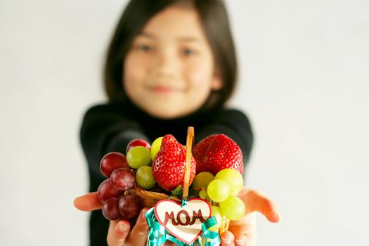 Little biracial asian girl holding fruit basket for mom. Focus on basket
