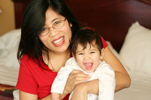 Asian mother sitting with baby boy on bed, smiling, waking up