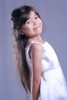 Beautiful little girl in white satin gown twirling playfully. Part Asian, Scandinavian background.