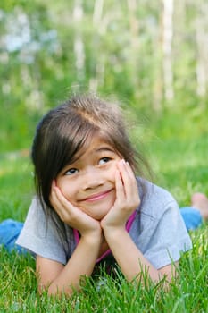 Child lying on grass with a thoughtful expression. Part asian, scandinavian background.