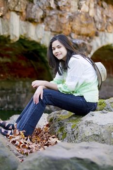 Biracial teen girl relaxing on rocks by stone bridge