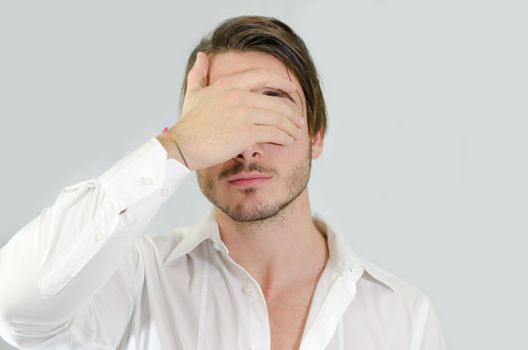 Attractive young man covering eyes with his hand