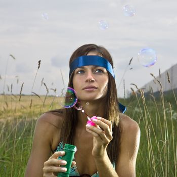 thoughtful young woman blowing soap bubbles in summer day