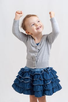 portrait of an smiling little blonde girl wearing a blue skirt holding up her hands
