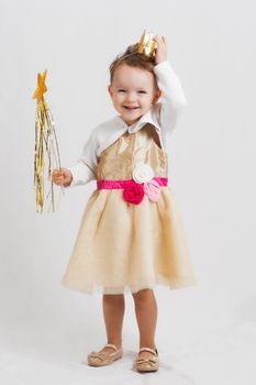 portrait of an happy smiling and laughing little blonde girl with a crown wearing a princess costume and holding a wand
