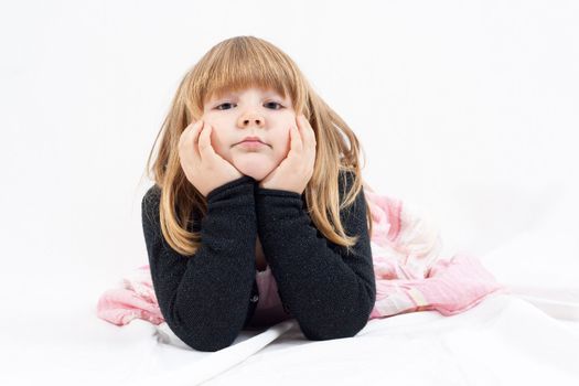 little blonde girl lie on a white blanket and looking bored into camera