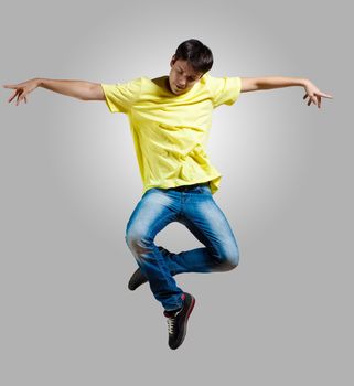 Modern slim hip-hop style man jumping dancing on a grey background