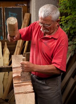 Old woodcarver working with mallet and chisel 2