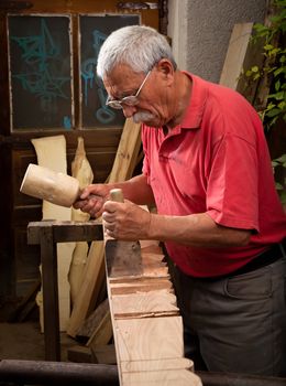 Old woodcarver working with mallet and chisel