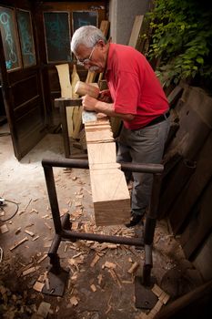 Old woodcarver working with mallet and chisel