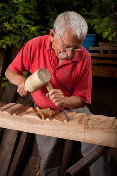 Old woodcarver working with mallet and chisel