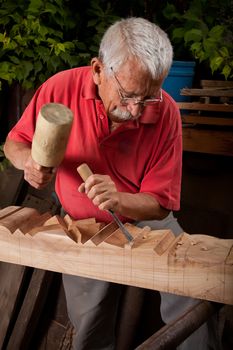 Old woodcarver working with mallet and chisel