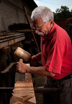 Old woodcarver working with mallet and chisel