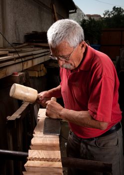 Old woodcarver working with mallet and chisel